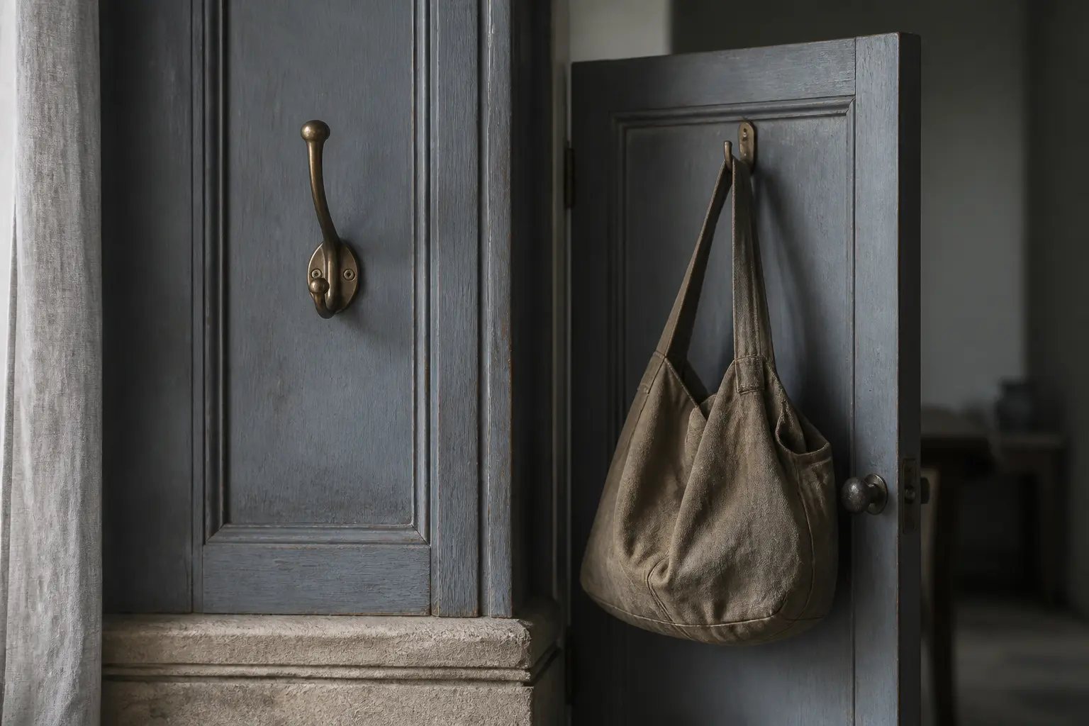 A brass coat hook hangs unused on the main slate-blue door; the work bag hangs on a narrower second door